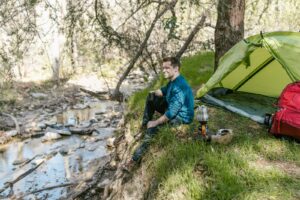 Un homme profite d'un voyage de camping serein au bord d'un ruisseau, entouré par la nature.