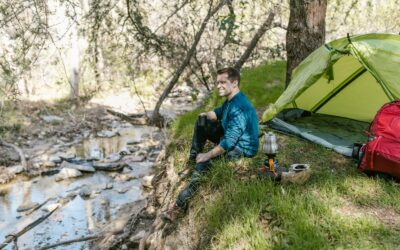 Un homme profite d'un voyage de camping serein au bord d'un ruisseau, entouré par la nature.